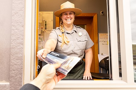 a park ranger handing a brochure to someone in a vehicle at an entrance station