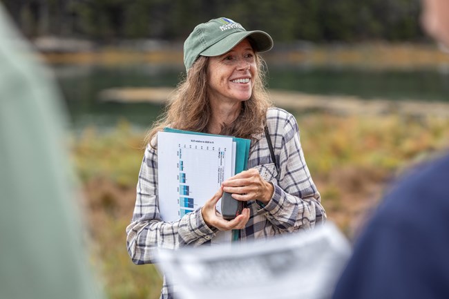 Woman smiles in front of a crowd while holding a series of scientific papers.