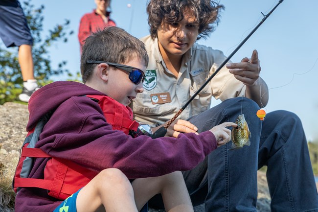 Intern helping kid take a fish off their line