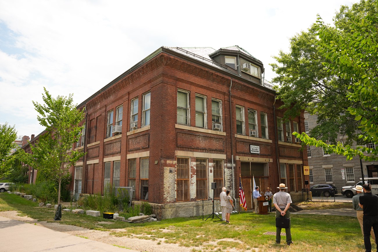 A three-story brick building, with the first two stories having paned windows and the third story as part of an arched roof.