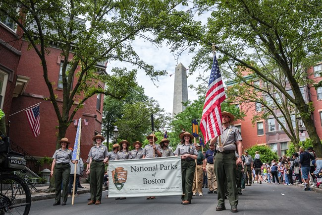 NPS uniformed rangers and volunters march with the Bunker Hill Monument in the background