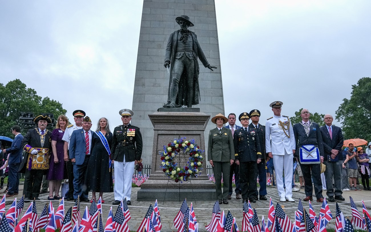 dignitaries in suits or uniforms around the William Prescott statue with a wreath
