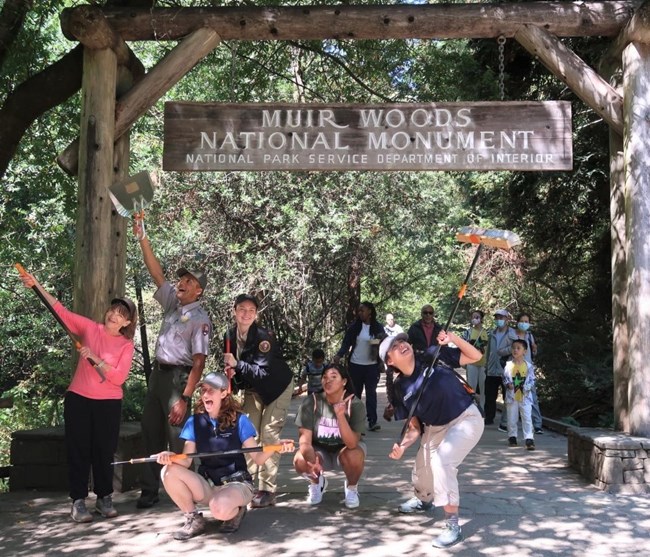 A group photo of volunteers and a park ranger posing a silly photo under the park entrance sign after a National Public Lands Day event at Muir Woods National Monument.
