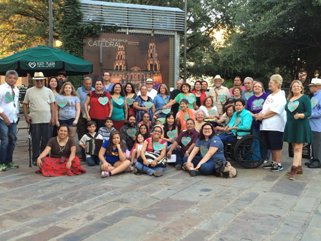 Around two dozen people pose in three rows holding light blue heart cut outs