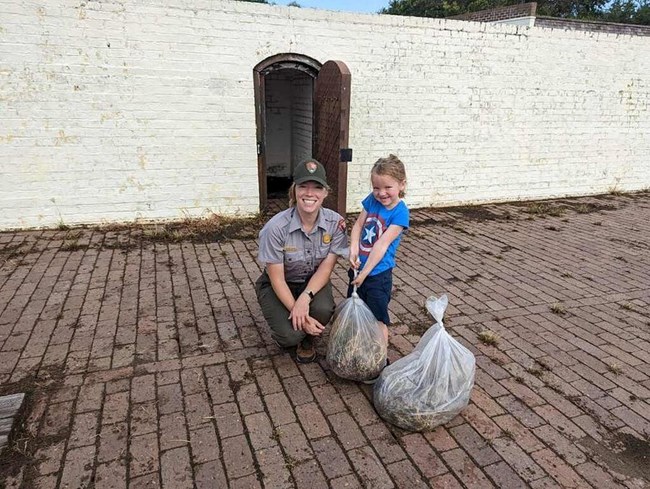 Two women together; one on the right side is picking up trash