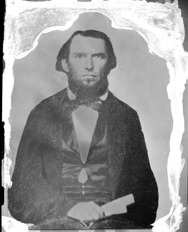 Historic portrait of Isaac Ebey- a man with shoulder length hair, a beard and a suit