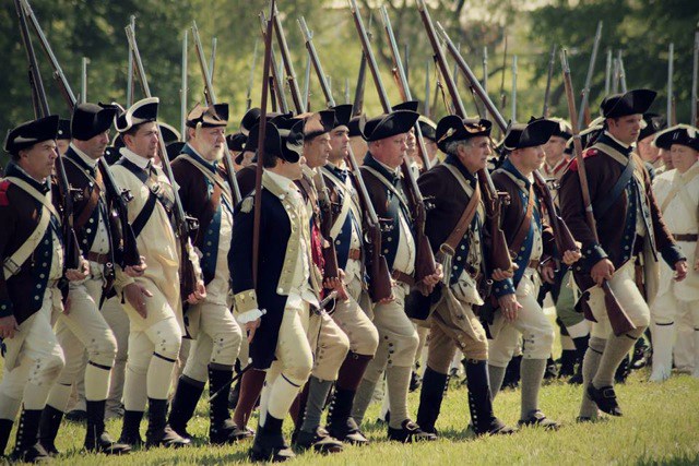 A well-ordered firing line of American soldiers, well equipped, in Revolutionary War uniforms.