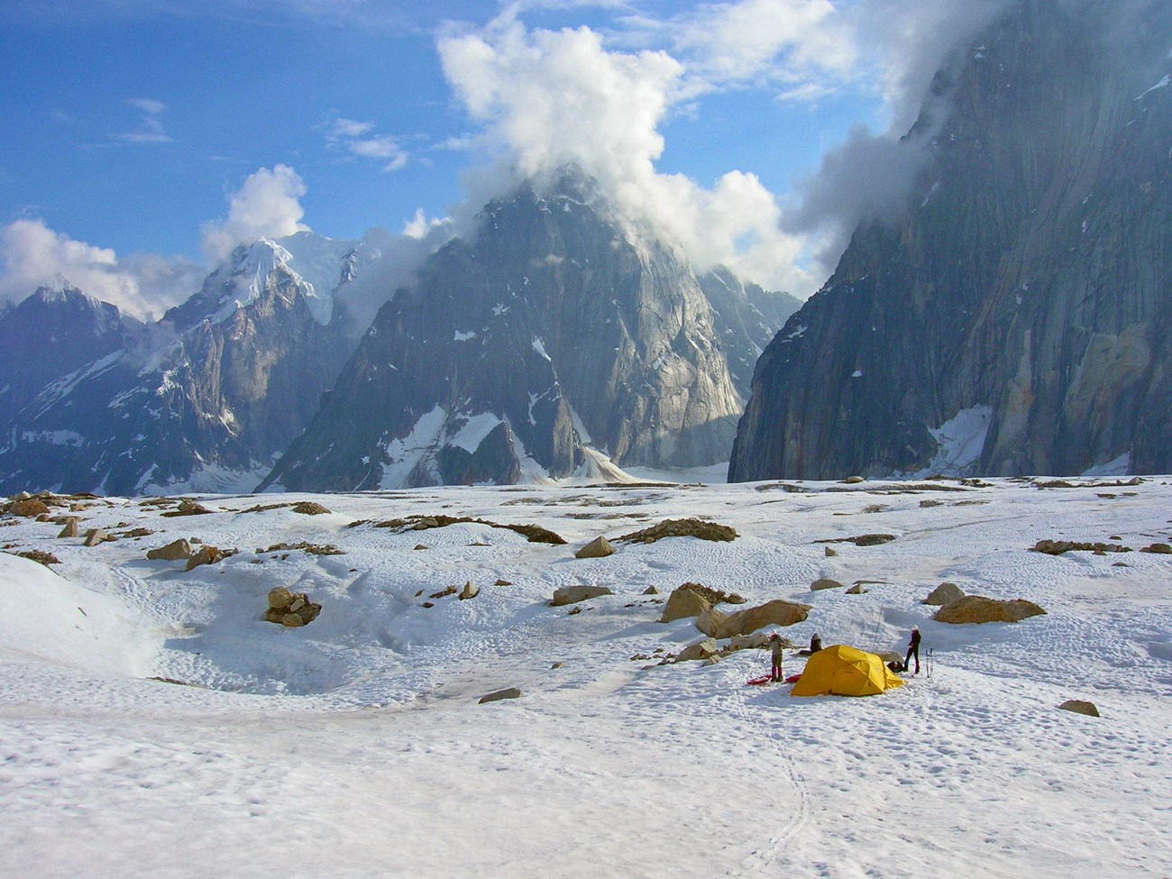 Tents dot a snowy field, sheer-sided mountains rising in the distance.