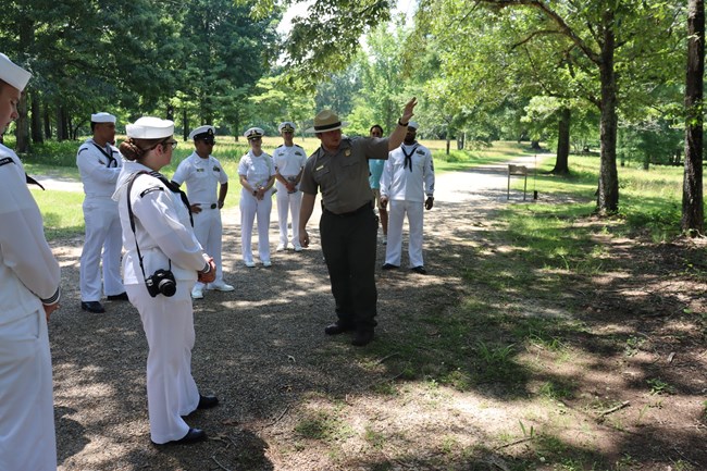 Park ranger points to something on the battlefield when speaking to sailors in white