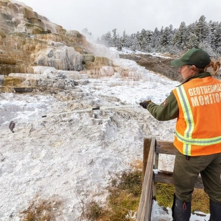a park ranger using a long extendable grabber to retrieve a hat from a thermal feature