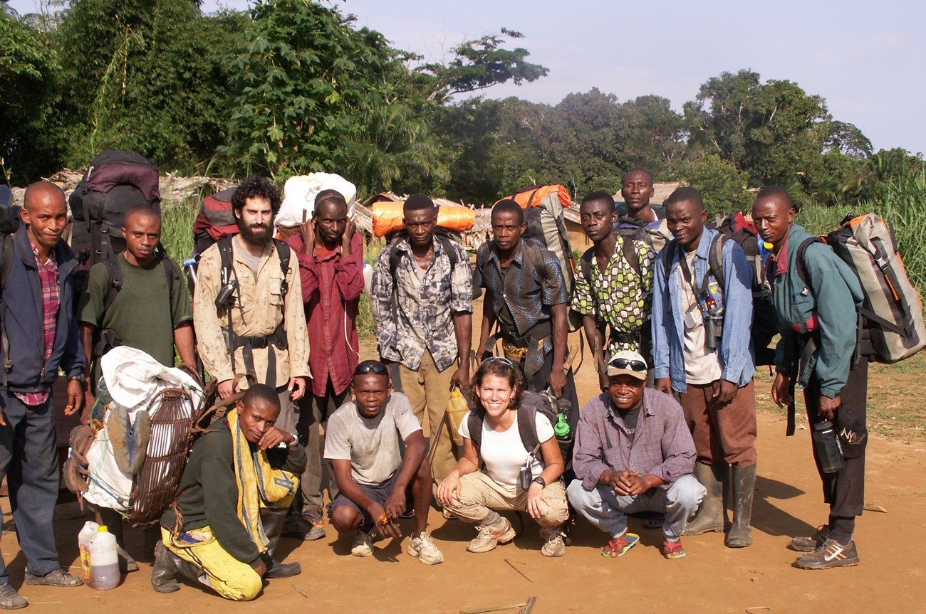 Jena and more than a dozen other people carrying packs and posing for a picture at the edge of a forest