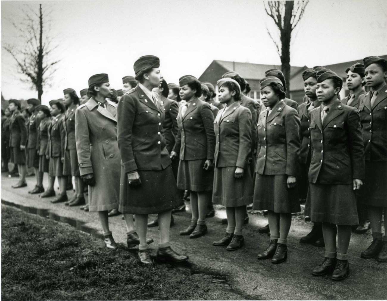 Black and white photo of two African American women officers inspecting African American women soldiers during WW2. They are all wearing WW2 Military uniforms.