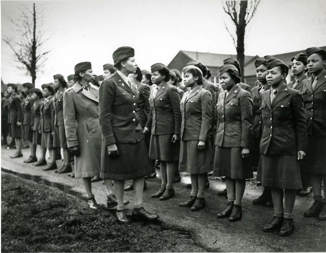 African American women in military uniforms; two are inspecting several rows of women