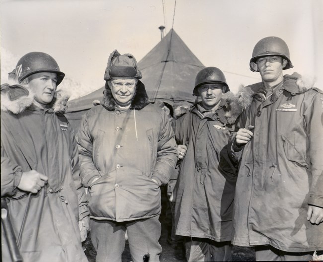 A black and white image showing President-elect Eisenhower with several soldiers, all wearing winter coats