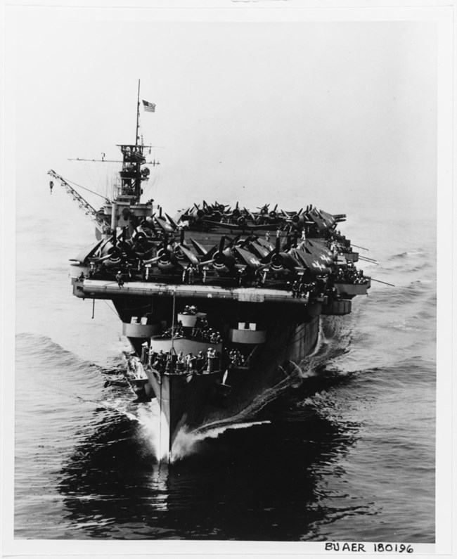 Black and white image of an aircraft carrier with many planes on the deck.