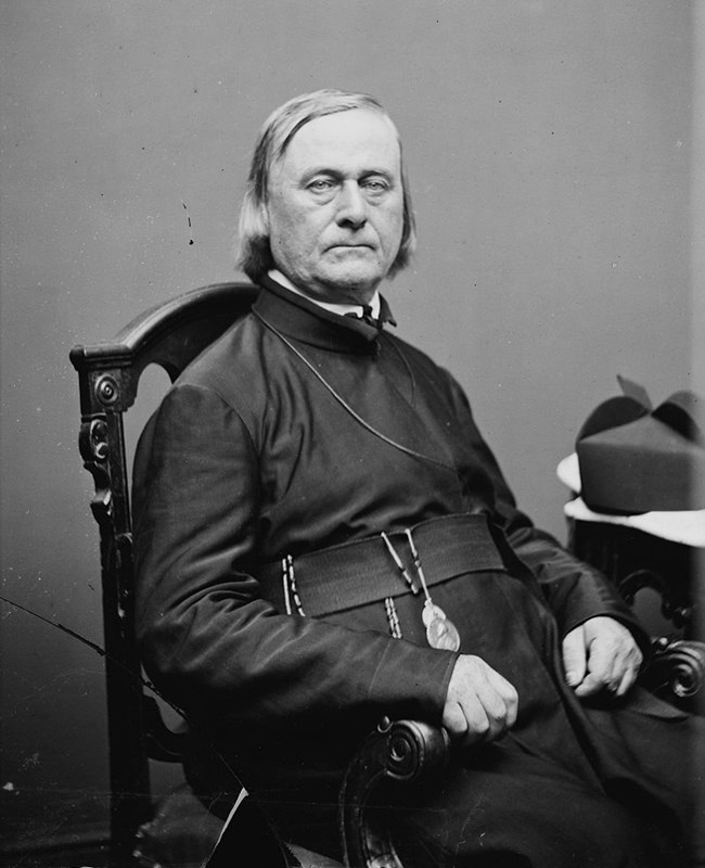 A black and white image of a man in a black robe sitting in a chair.