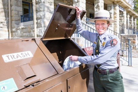 a park ranger throwing trash into a trash can