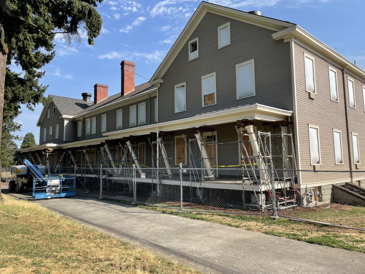 Building 993, a grey building with cream colored trim. The structure is three stories, with a long façade and squared angles, with has a large porch. The porch roof is supported by metal bracing while columns lean at an angle during the work.