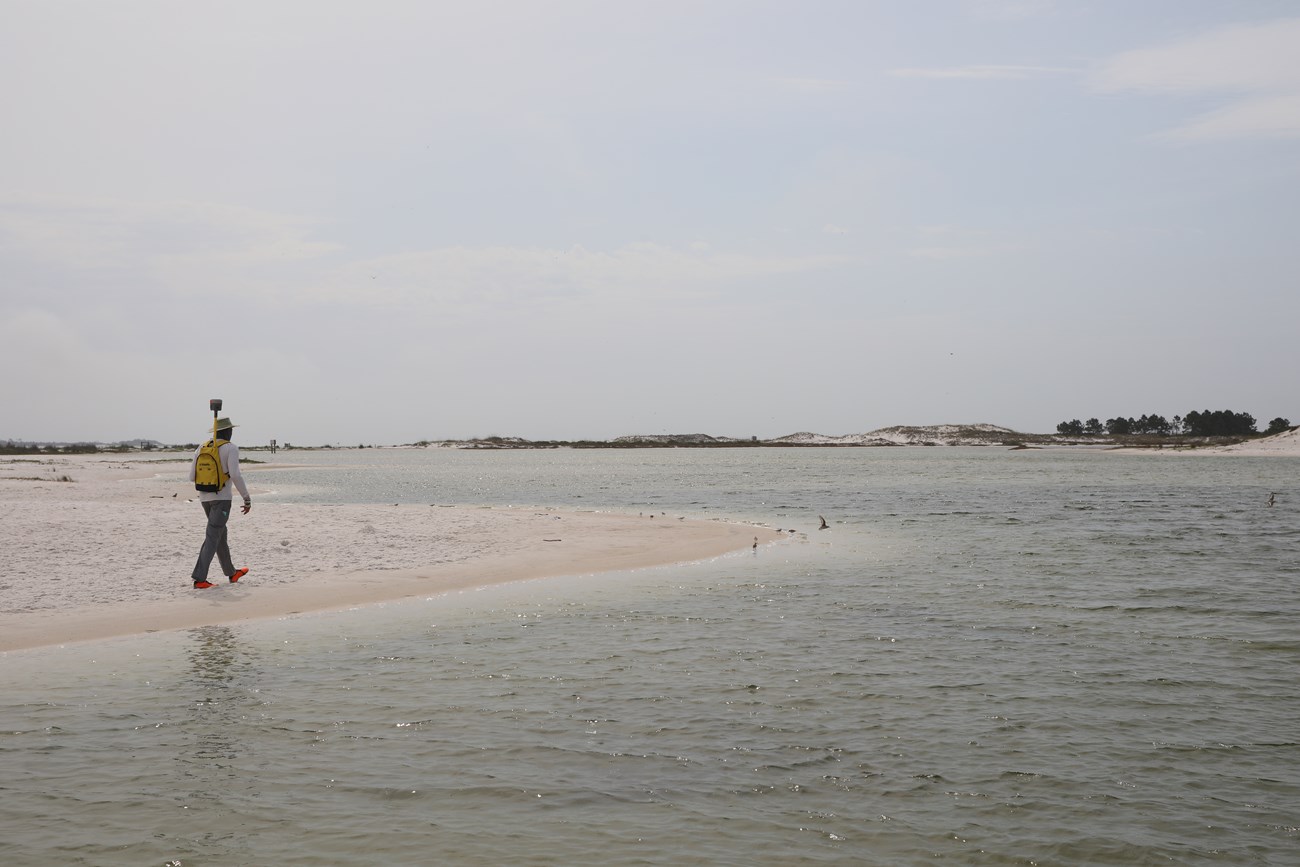 Surveyor with GPS equipment walking along the sandy shoreline
