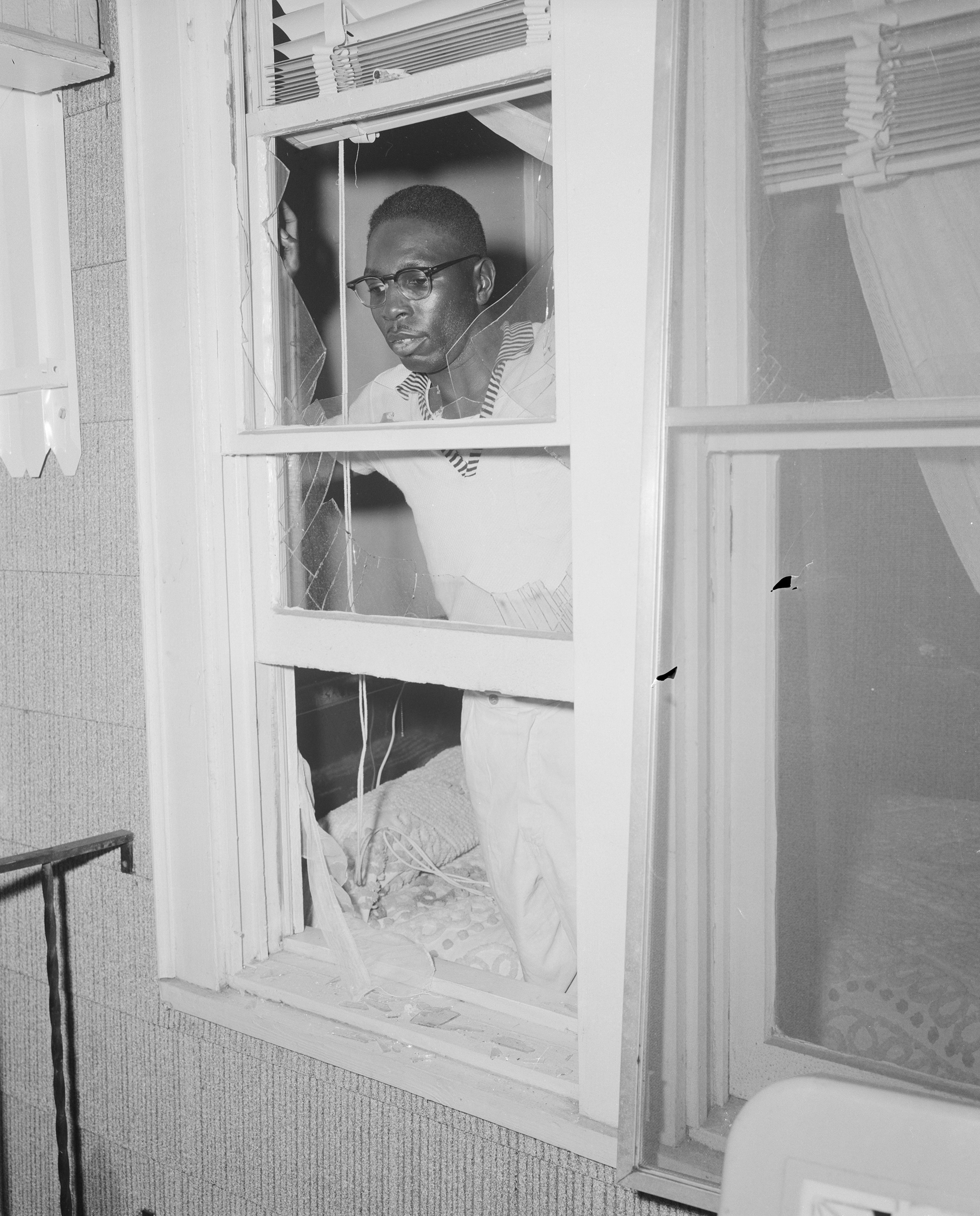 A man looks through a broken window from inside his home.