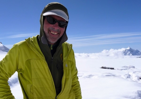 A man in a yellow-green jacket stands on a mountain summit above the clouds.