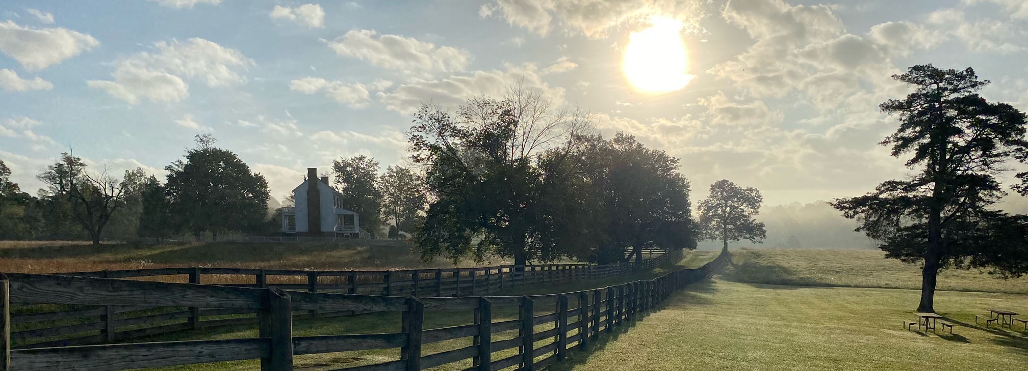 A white farm house and black fence with the sun in the background