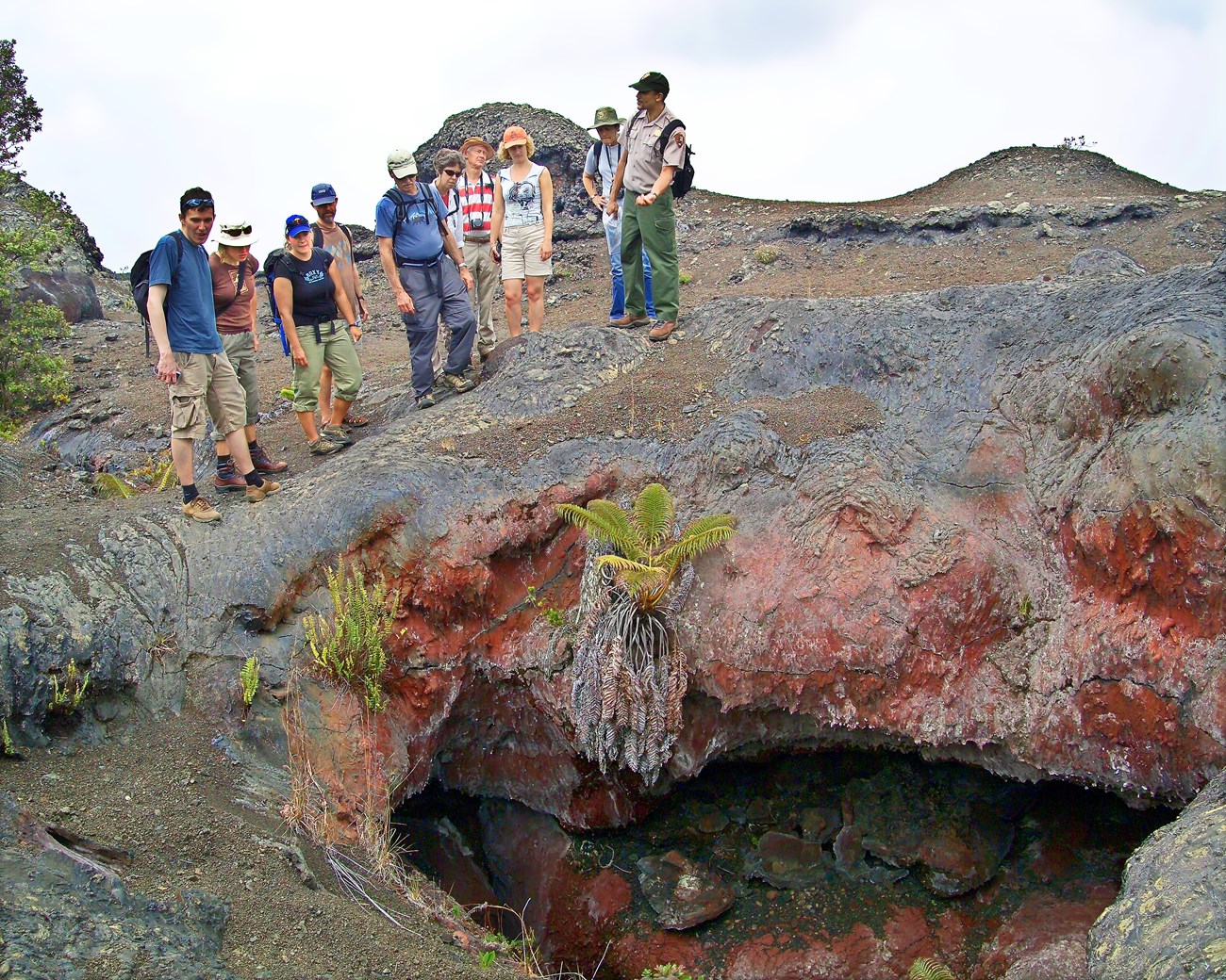 National Park Service ranger talking and gesturing to a group of visitors about a fissure in the lava rock beneath them.