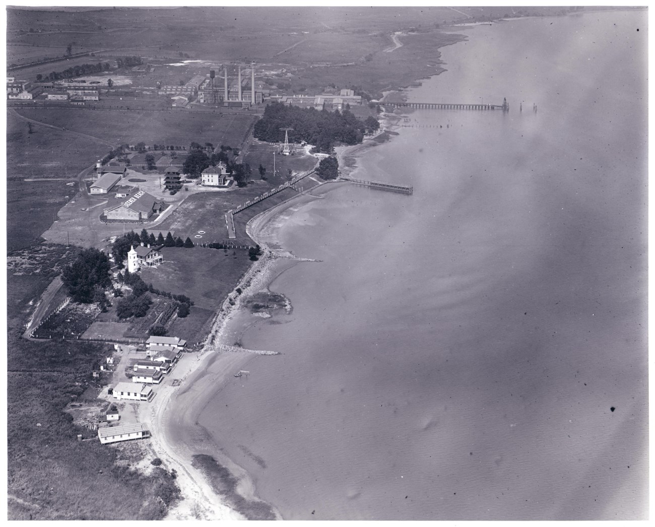Black and white photo from an aerial perspective of a beach with buildings on the land.