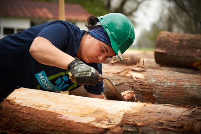 A member of the HOPE Crew shaves down a timber.