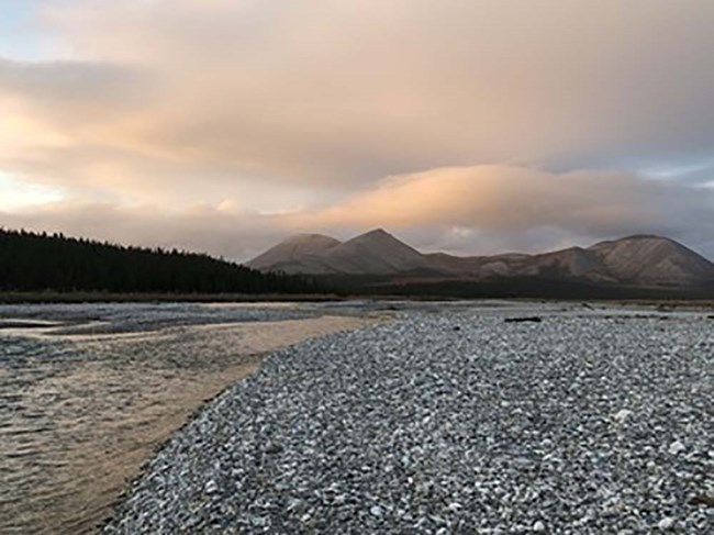 An Arctic stream, gravel beach, and mountains in the background.