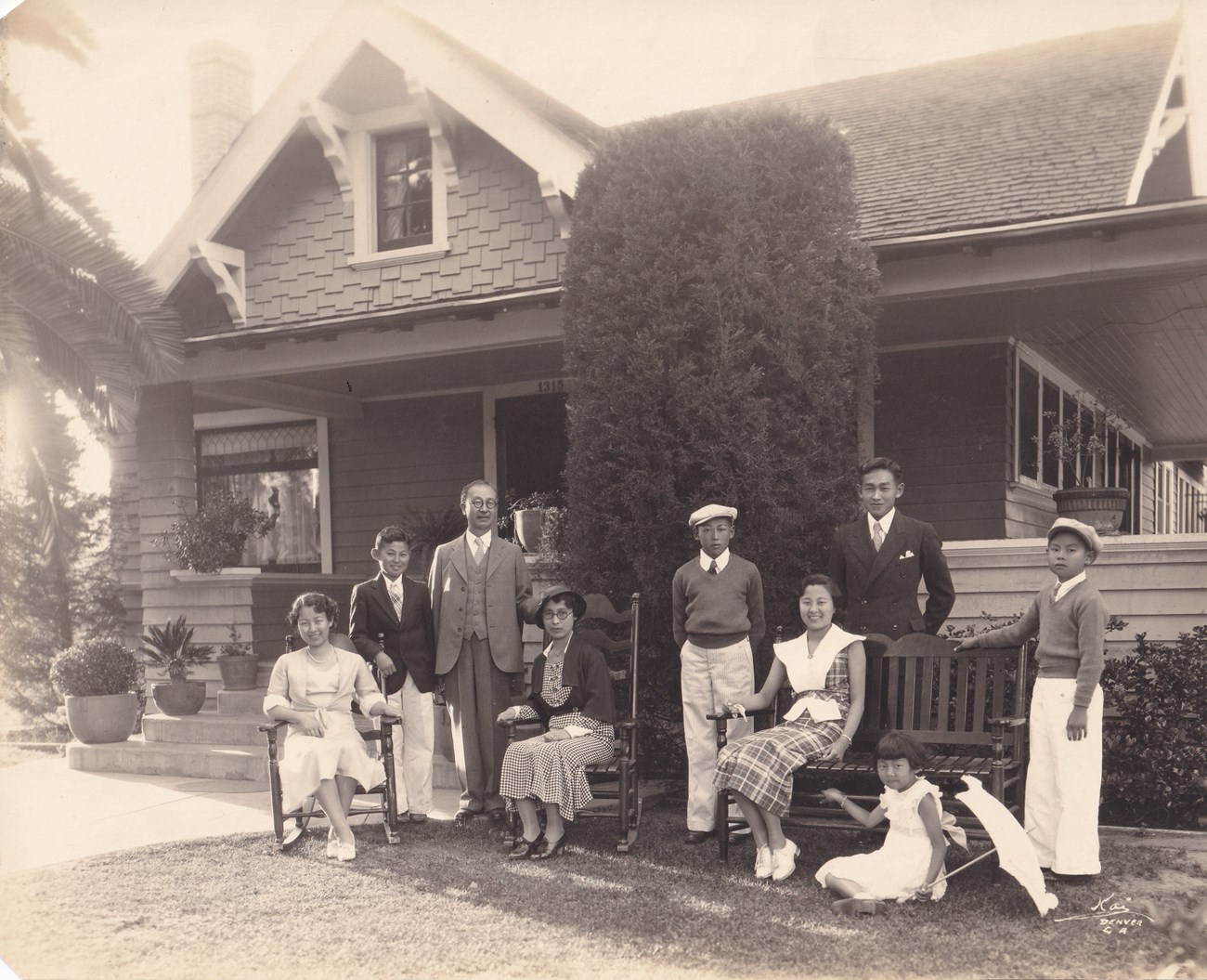 A large family (four boys, four girls, mother, and father) standing in front of a large house.