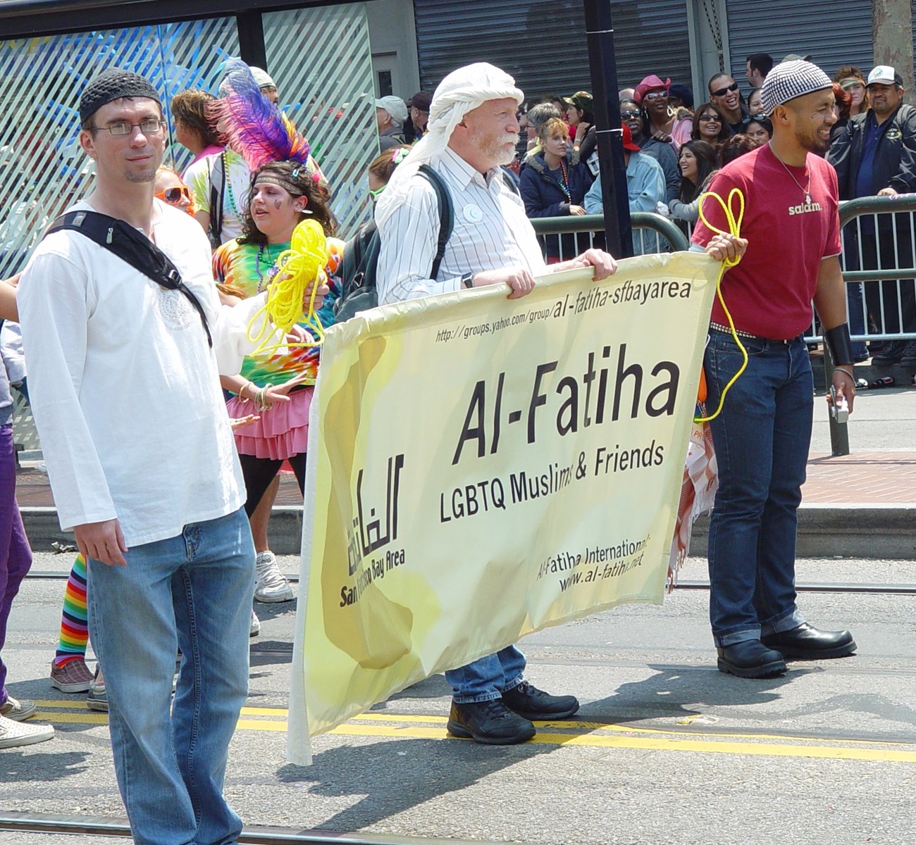 People marching in a Pride Parade. They have a sign that says, "LGBTQ Muslims and Friends."