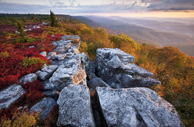 A photo of flat rock outcrop peaks with red and gold covered mountains behind.