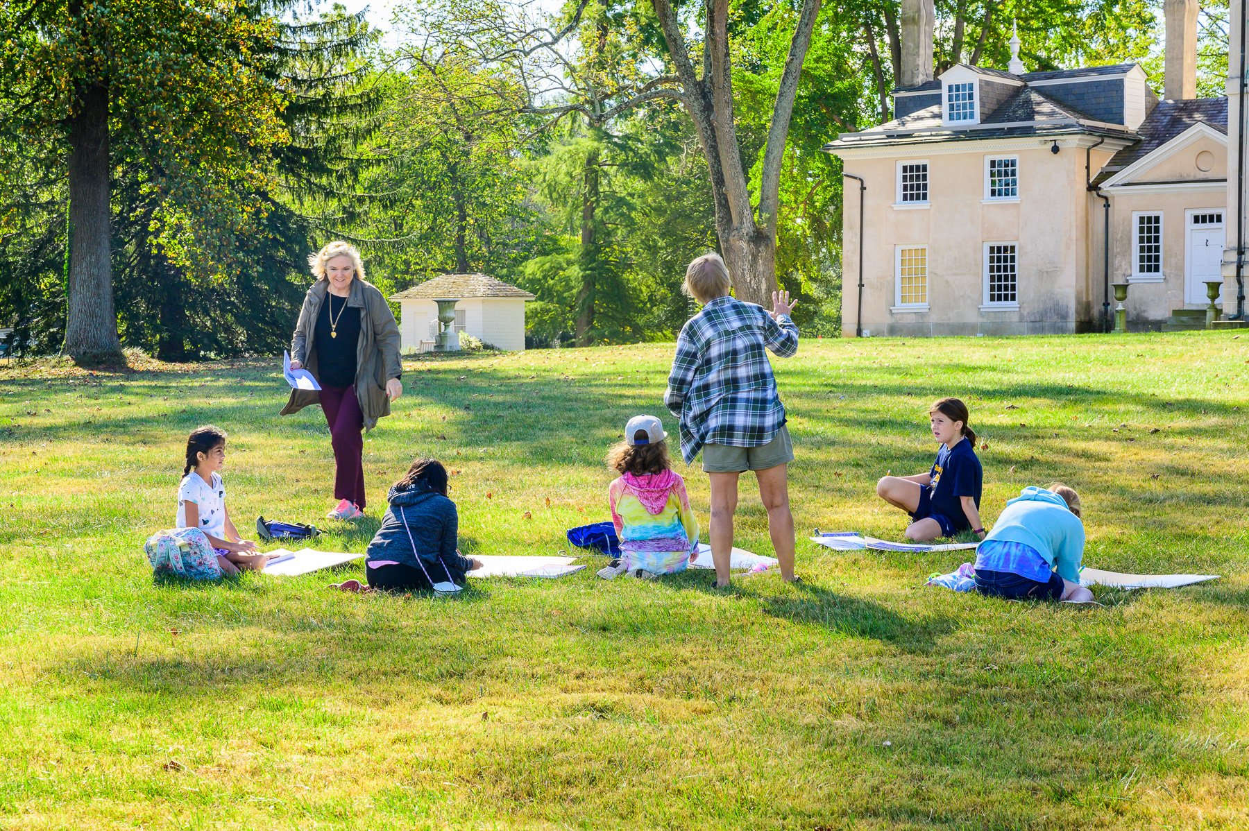 Young visitors listening to Ann speak in front of the mansion