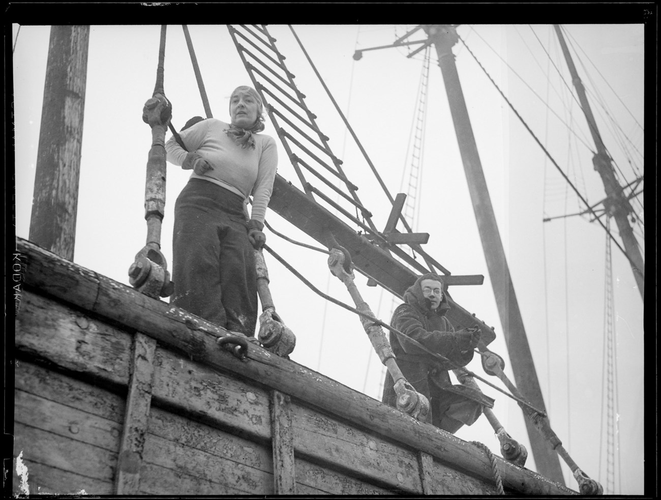 looking up at a young man and woman standing on the edge of a ship holding on to ropes.