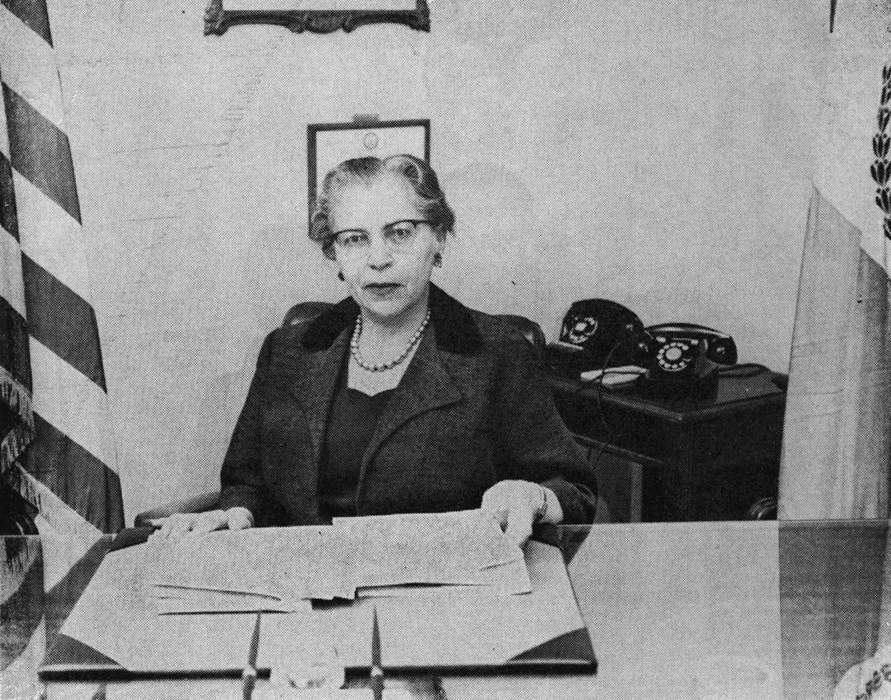 Black and white image of woman sitting at a desk with an open book.