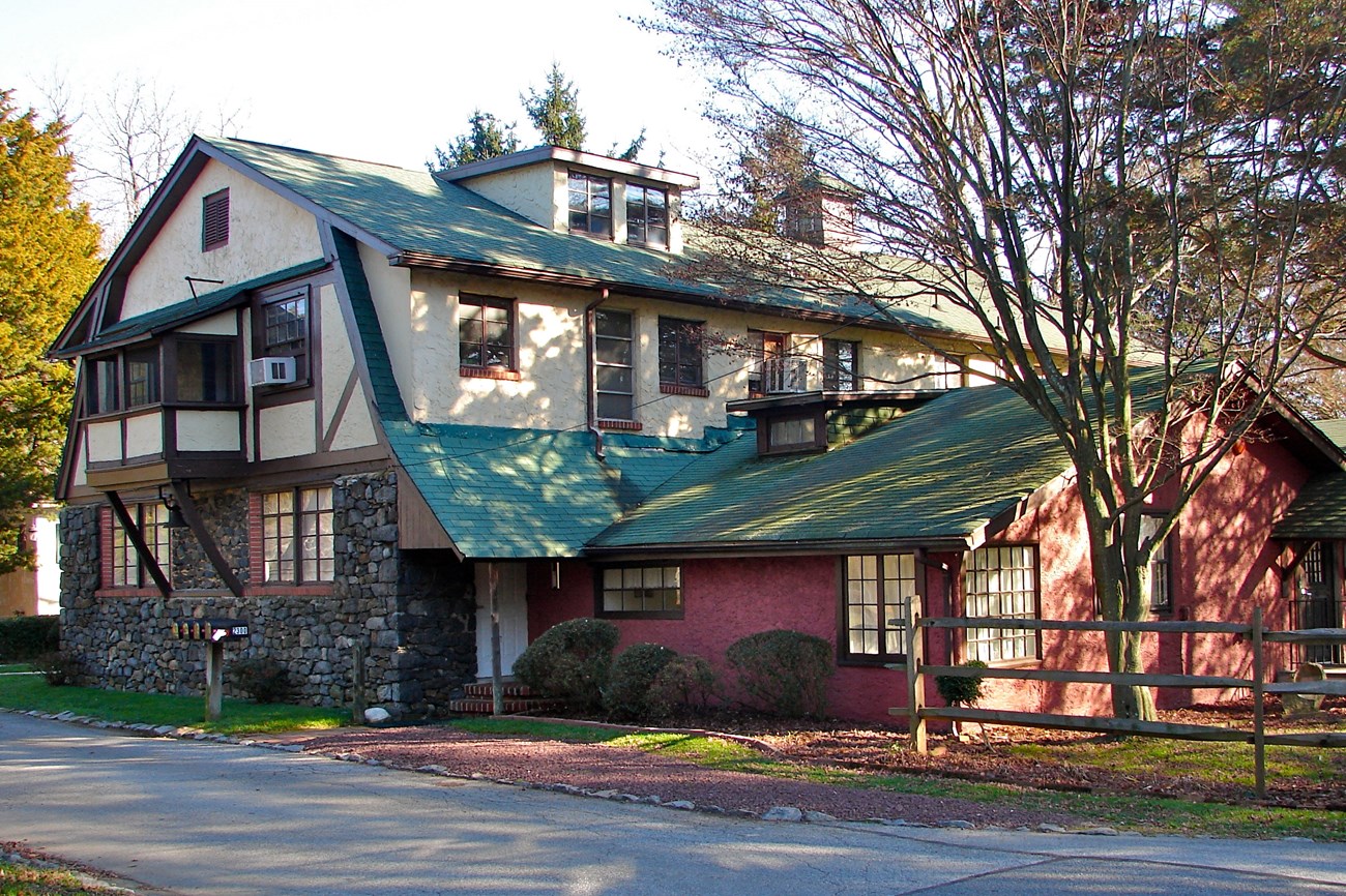 two story Germanic style building, stone first floor, tan second floor and a green roof with a red one story extension to the right