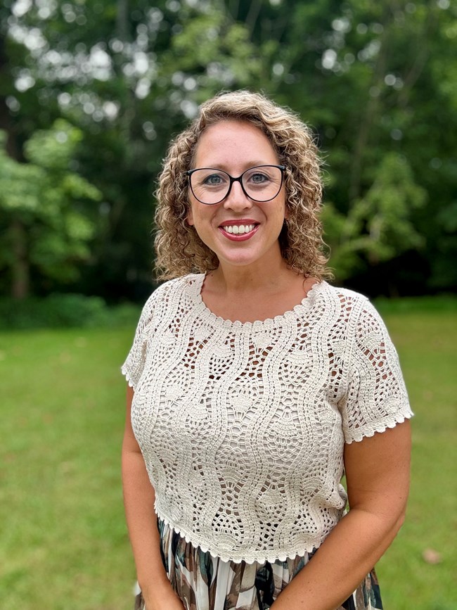 A woman with curly hair and glasses smiles for the camera.