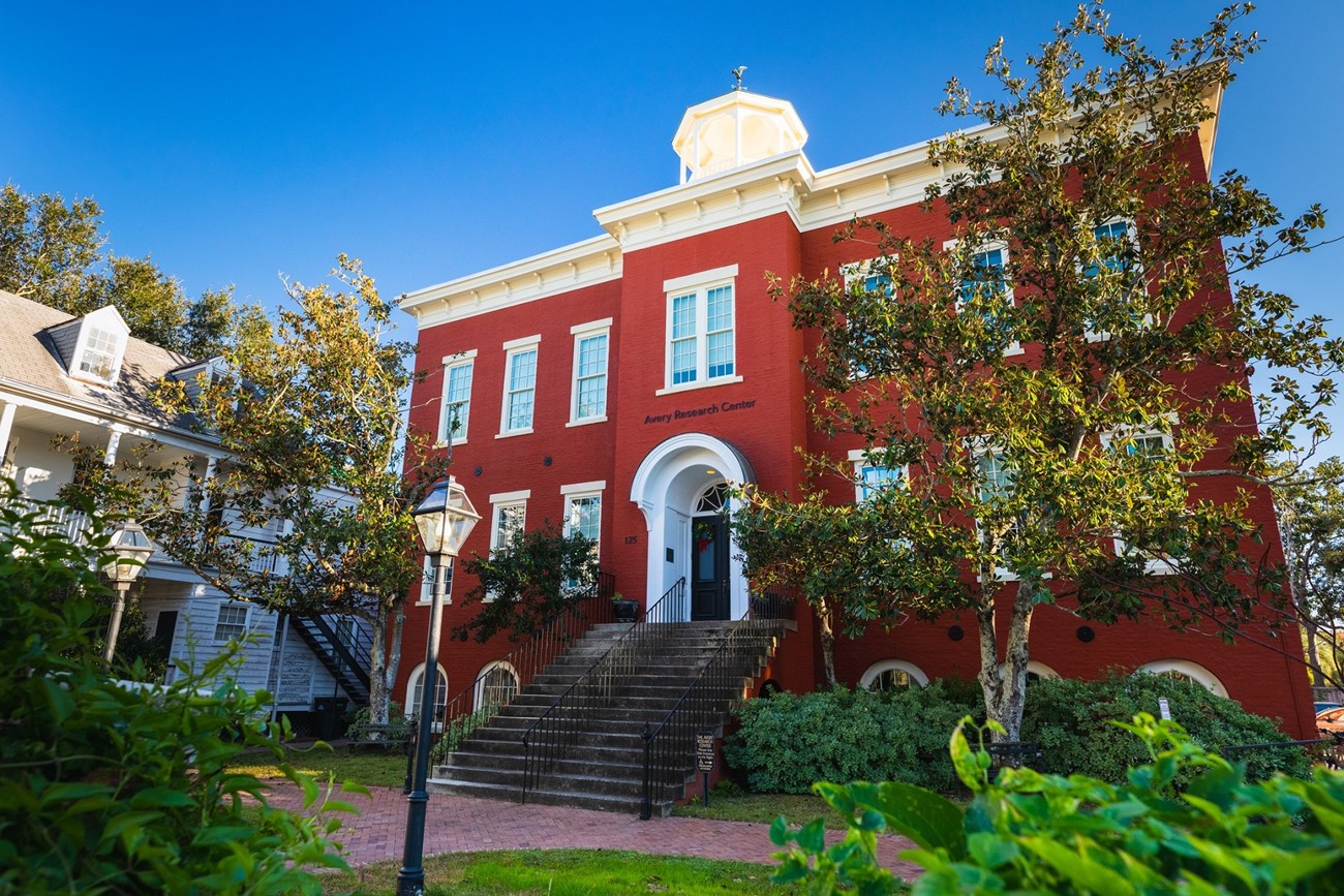 three story red brick school building with cupola on top and front steps leading up to large door on second level