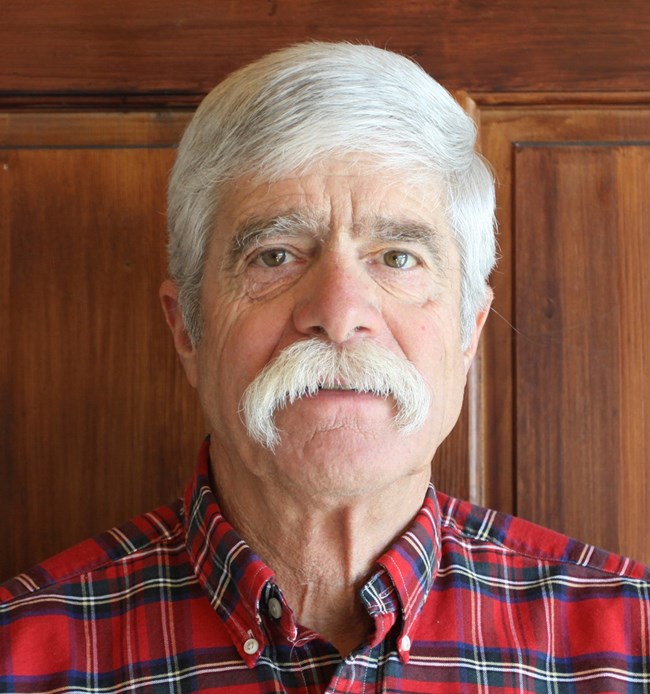 A man with gray hair and gray mustache is seen from shoulders up.
