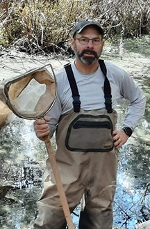 man wearing waders and a ball cap holding a fishing net