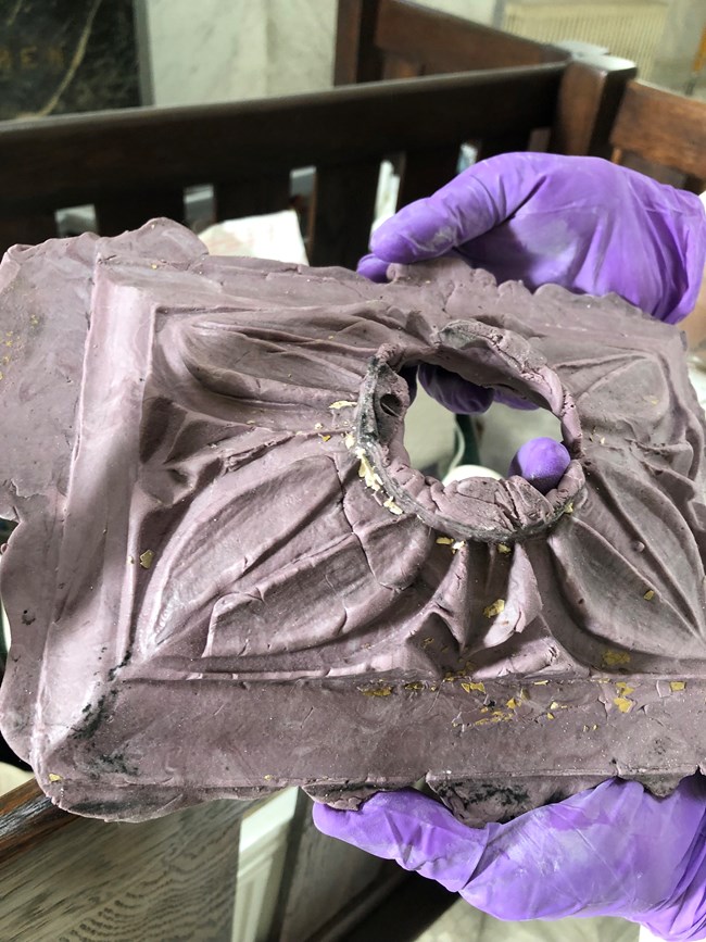 Someone with purple gloves holding a plaster mold of a floral medallion.