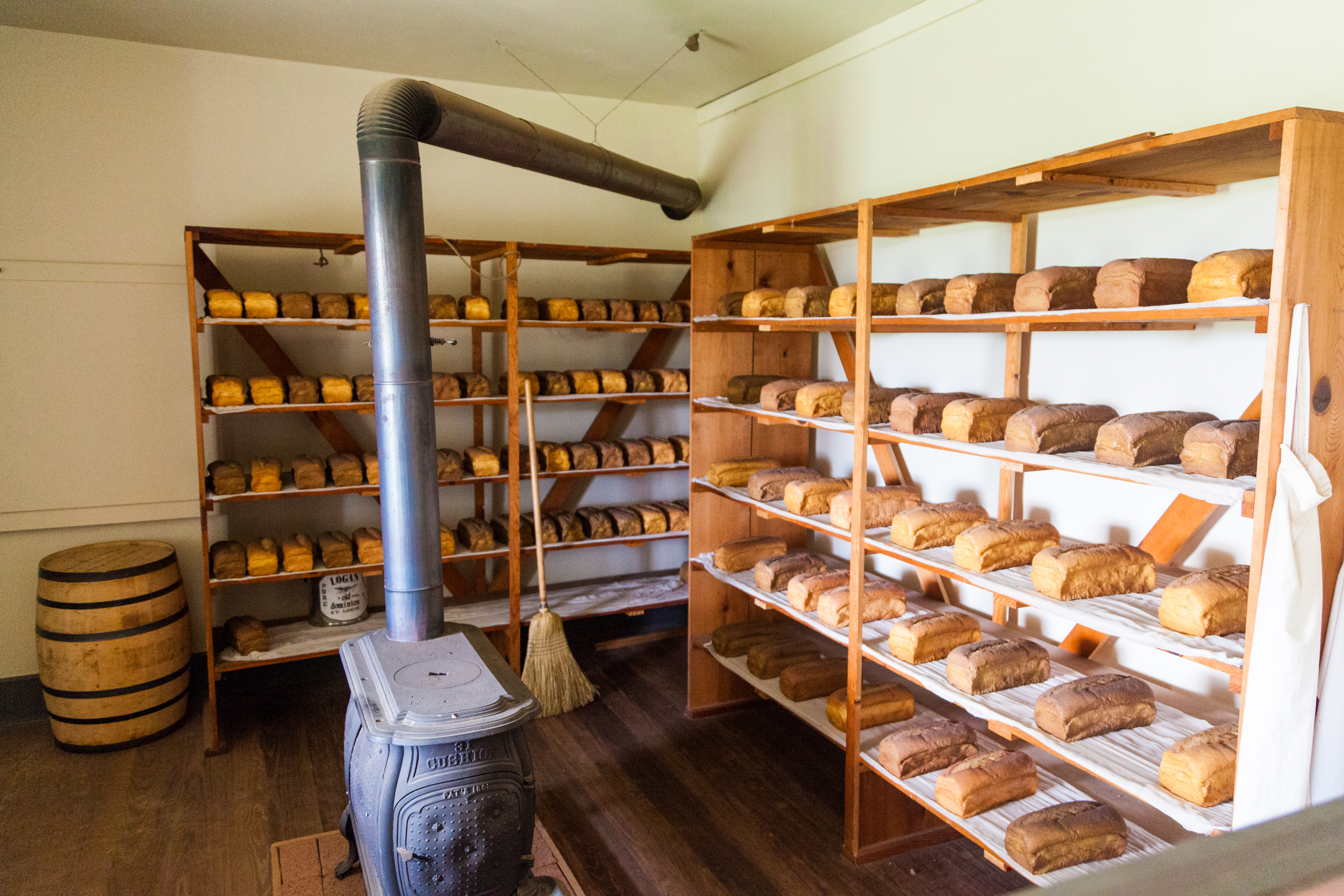 Room with unpainted wood floor, two wooden shelves filled with bread.