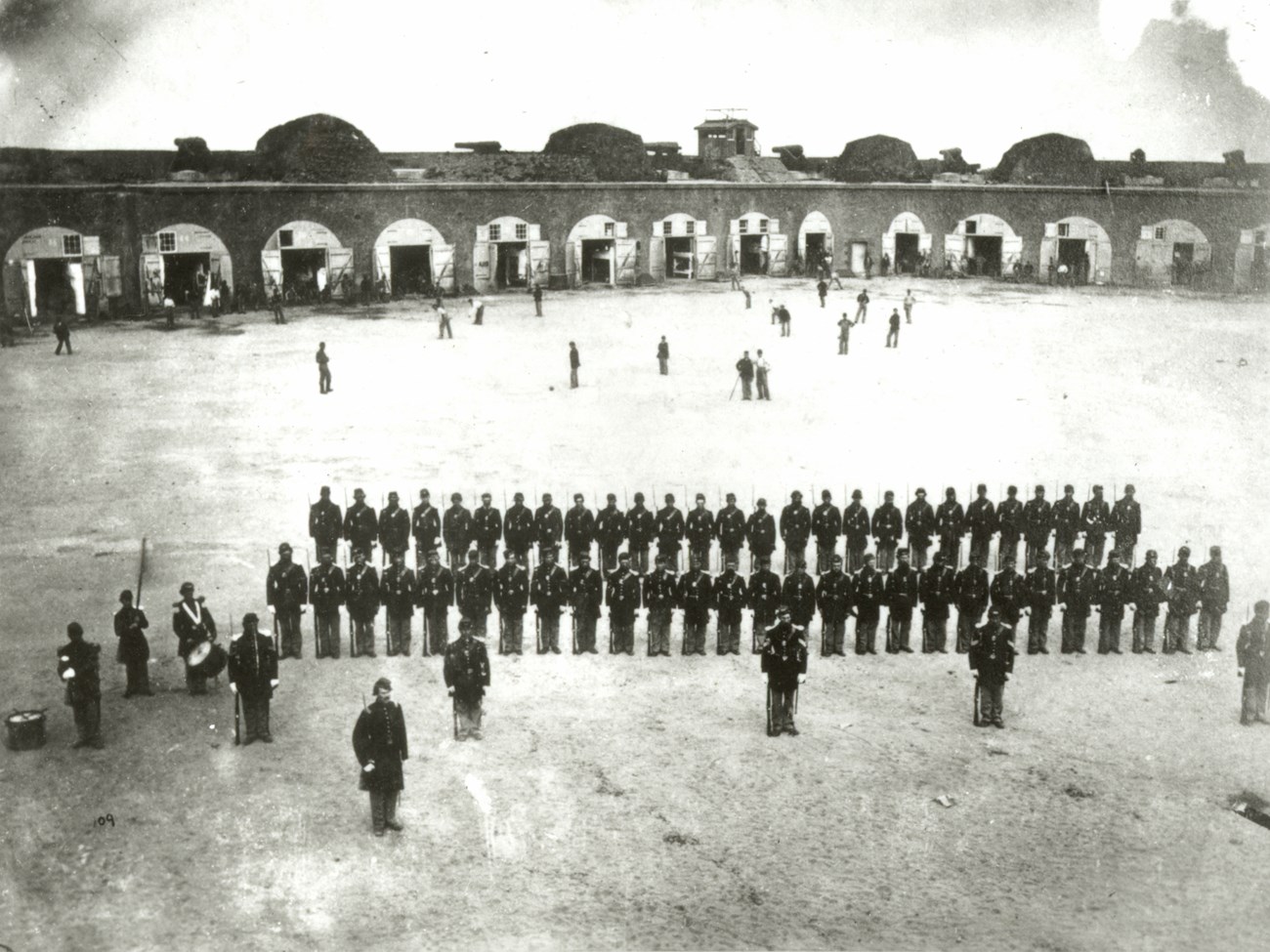 Two lines of soldiers with a group of men playing baseball in the rear.