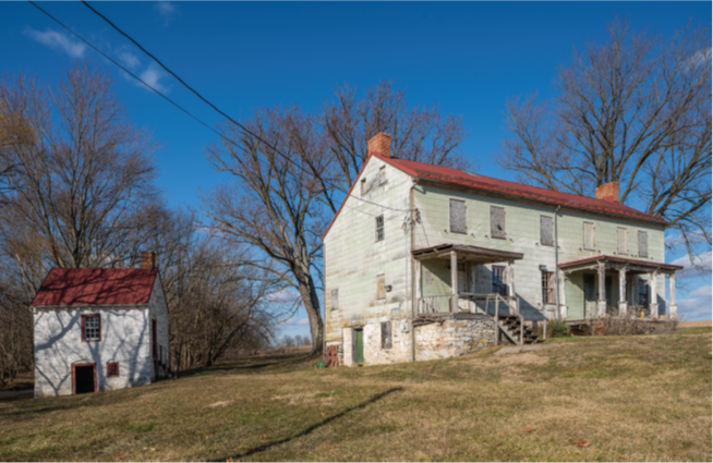 HABS photograph showing a split-level wood farm house on a hill with a stone foundation, red roof and brick chimneys. A smaller stone smokehouse painted white is to the left.
