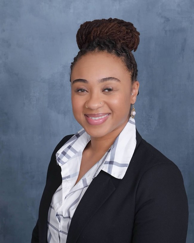 Headshot of a Black woman wearing a blue and white collared shirt and black suit jacket.