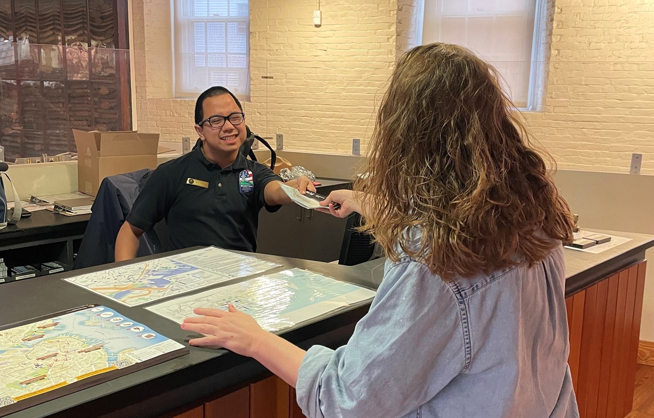 A young man speaking with a woman and handing over a brochure.