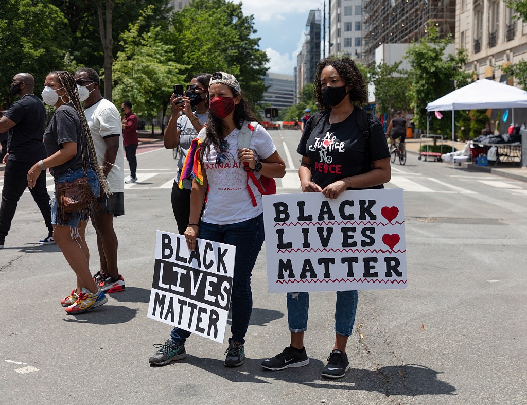 Two women wearing facemasks and carrying posterboard signs that read Black Lives Matter