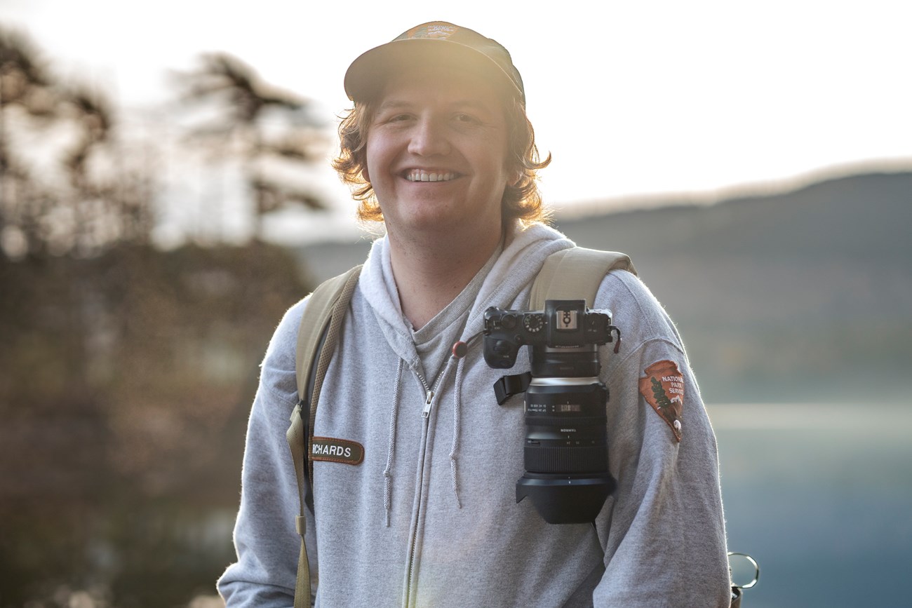 Park ranger wearing a camera backpack in front of Eagle Lake.