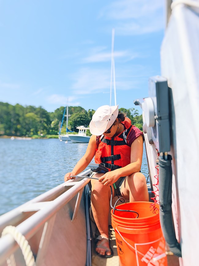 Female scientist sits on boat bench and collects water quality data in one of the monitored salt ponds.